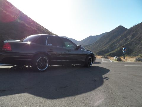 2003 Ford Crown Victoria - Rear quarter of a black sedan in a hillside parking area, dry mountains and a person in the distance