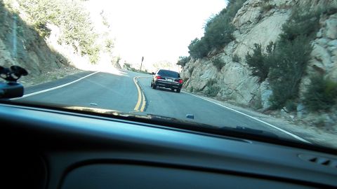 2003 Ford Crown Victoria - Driver POV following a dark sedan around a bend on a mountain road beside a rock cut