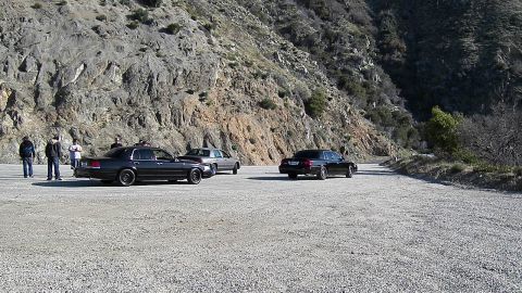 2003 Ford Crown Victoria - Several full-size sedans spread across a dirt mountain pullout with a small group at left