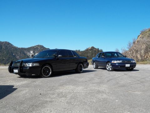 2003 Ford Crown Victoria - Front three-quarter view of a black sedan and a blue sedan in a gravel mountain pullout