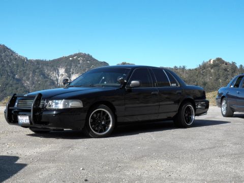 2003 Ford Crown Victoria - Murdered-out sedan with grille guard and tinted windows on dark wheels, ridge behind