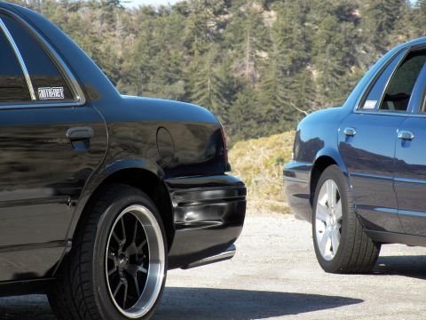2003 Ford Crown Victoria - Close rear view of black sedan with staggered wheels facing a silver full-size sedan