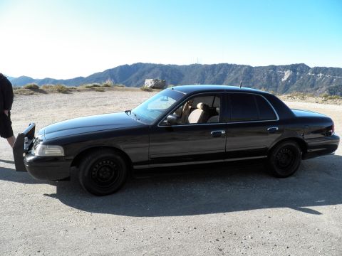 2003 Ford Crown Victoria - Side view of black full-size sedan on plain steel wheels, ridgeline filling the horizon