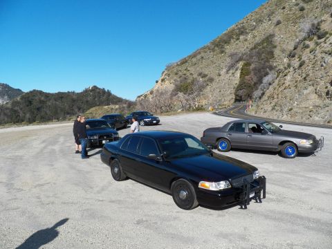 2003 Ford Crown Victoria - Black full-size sedan front and center among several sedans below a rocky ridge