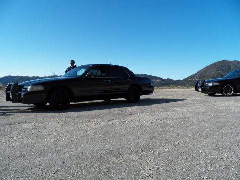 2003 Ford Crown Victoria - Side profile of a black police-style Crown Victoria, a second sedan parked at right.