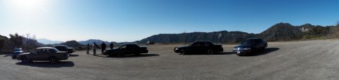 2003 Ford Crown Victoria - Wide panorama of a sedan meet on a dirt pullout ringed by mountain ridges.