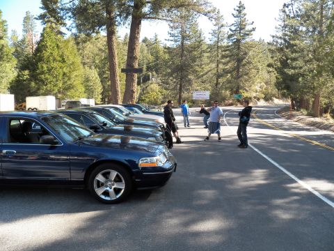2003 Ford Crown Victoria - Blue full-size sedan at curbside as people walk on a winding mountain road.