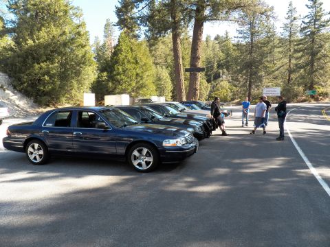 2003 Ford Crown Victoria - Blue full-size Mercury sedan heads a parked lineup with people standing nearby.