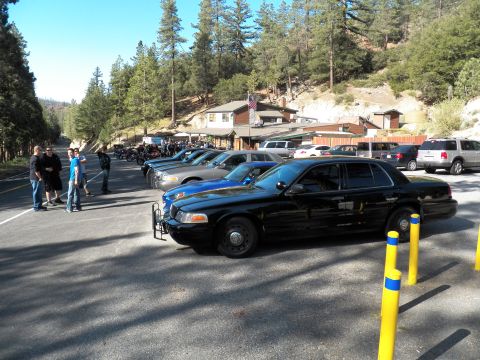 2003 Ford Crown Victoria - Blacked-out Crown Victoria leads a row of cars near a mountain lodge with flag.