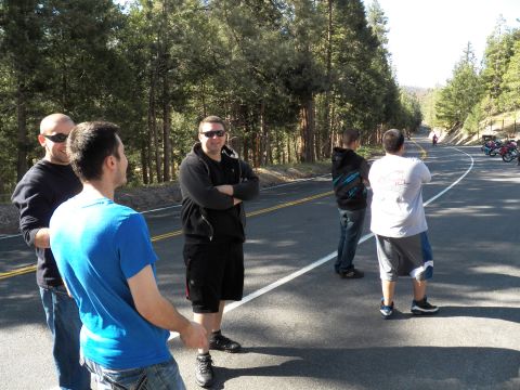 2003 Ford Crown Victoria - Five men talk roadside on a tree-lined mountain road, motorcycles in the distance.
