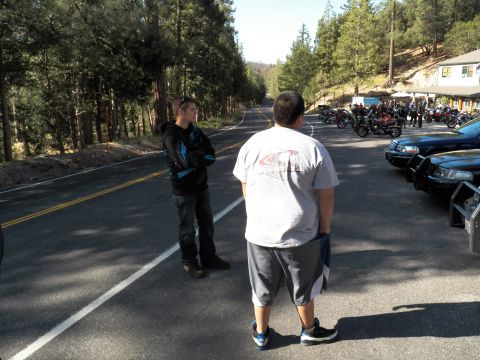 2003 Ford Crown Victoria - Two men talk on the roadway as bikes gather by a lodge and parked sedans.