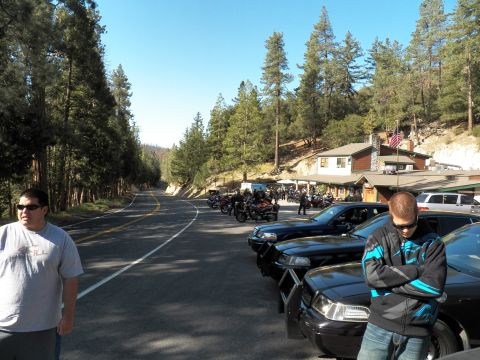 2003 Ford Crown Victoria - Two men wait by parked cars while bikes line a curving mountain road near a lodge.