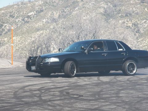 2003 Ford Crown Victoria - Driver visible inside a black push-bar sedan as it slides across the open burnout pad.