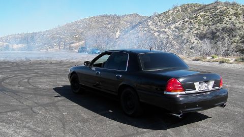 2003 Ford Crown Victoria - Blacked-out full-size sedan with twin exhaust tips sits on a skid-marked asphalt pad.