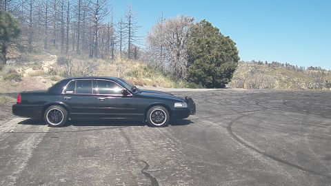 2003 Ford Crown Victoria - Side view of a blacked-out sedan at rest on a tire-streaked mountain burnout lot.