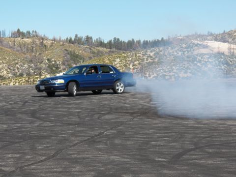 2003 Ford Crown Victoria - Blue four-door sedan slides through its own tire smoke on an open mountain burnout pad.