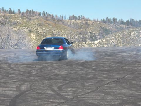 2003 Ford Crown Victoria - Rear view of a blue sedan spinning its tires with smoke rising on a mountain pullout