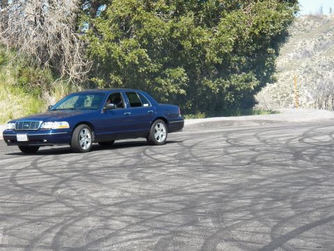 2003 Ford Crown Victoria - Side profile of a navy full-size sedan with tire marks curving across the pavement