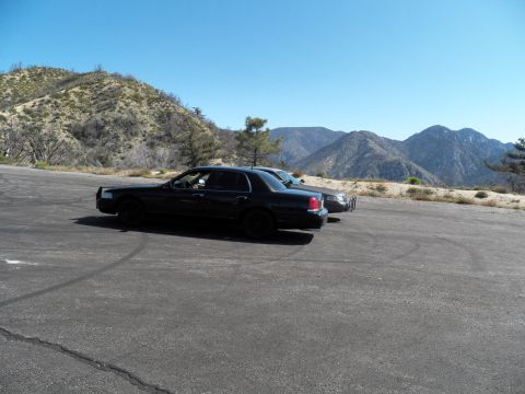 2003 Ford Crown Victoria - Side view of a black sedan on a paved pullout backed by rugged mountain ridges