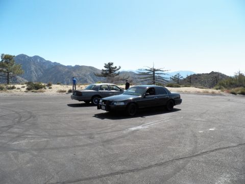 2003 Ford Crown Victoria - Two full-size sedans on a paved pullout as a person stands by the silver car