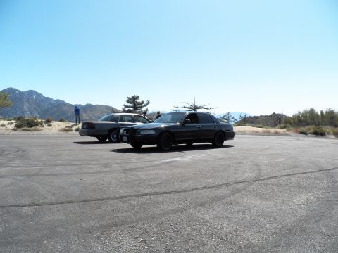2003 Ford Crown Victoria - black and a silver full-size sedan sit on a mountain clearing under blue sky