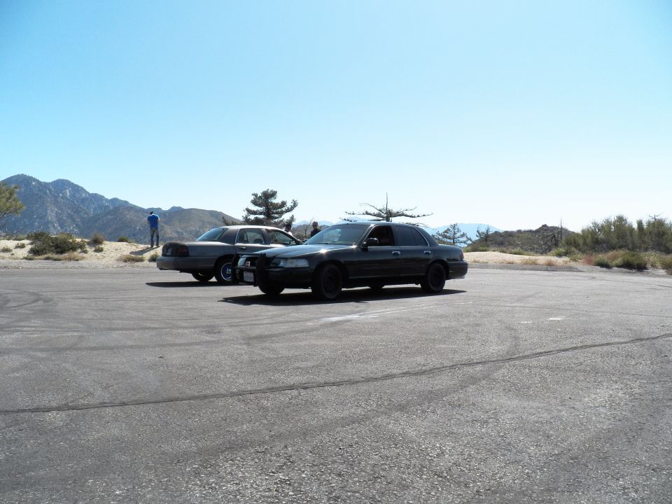 Two dark sedans parked on a wide asphalt lot with mountains behind