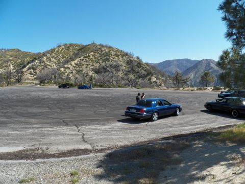 2003 Ford Crown Victoria - Several cars and two people gather on a wide paved pullout among the hills