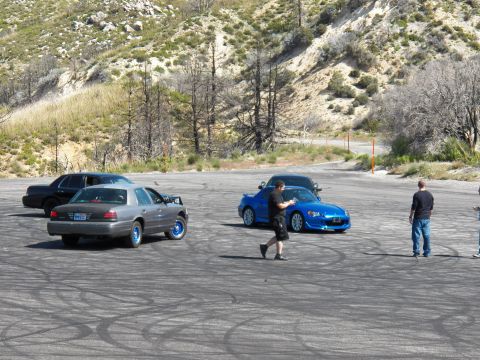 2003 Ford Crown Victoria - man walks toward a blue roadster beside a silver sedan with people watching
