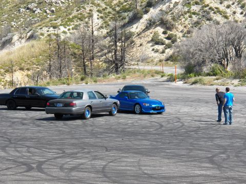 2003 Ford Crown Victoria - Three cars parked in a row on a mountain lot as two men talk at right