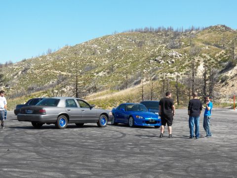 2003 Ford Crown Victoria - Two cars parked side by side on a hillside lot as people gather to talk