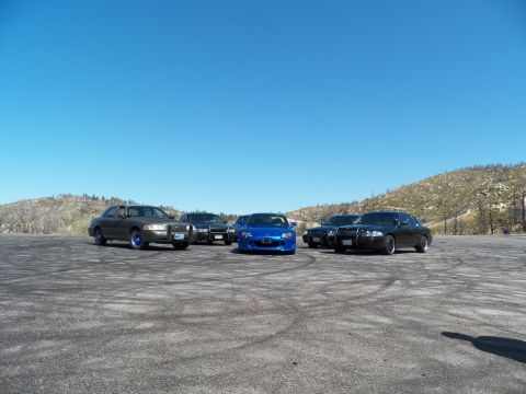 2003 Ford Crown Victoria - Spread-out car meetup: a blue roadster centered among grey and black sedans.