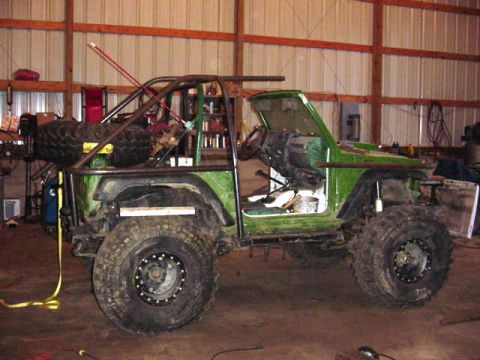 1992 Ford Bronco - Modified off-road vehicle with custom roll cage and large tires sits in a workshop.