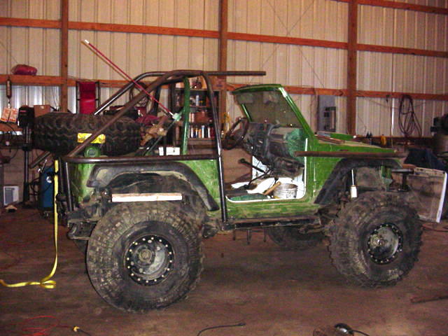 Green off-road vehicle with roll cage and large tires, in a garage. Doors removed, interior visible