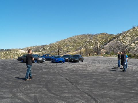 2003 Ford Crown Victoria - Wide shot of a small car meetup with people and a blue roadster among sedans.