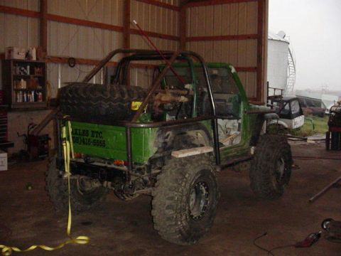 1992 Ford Bronco - A heavily modified green off-road vehicle sits inside a garage, showing its custom roll cage and large tires.