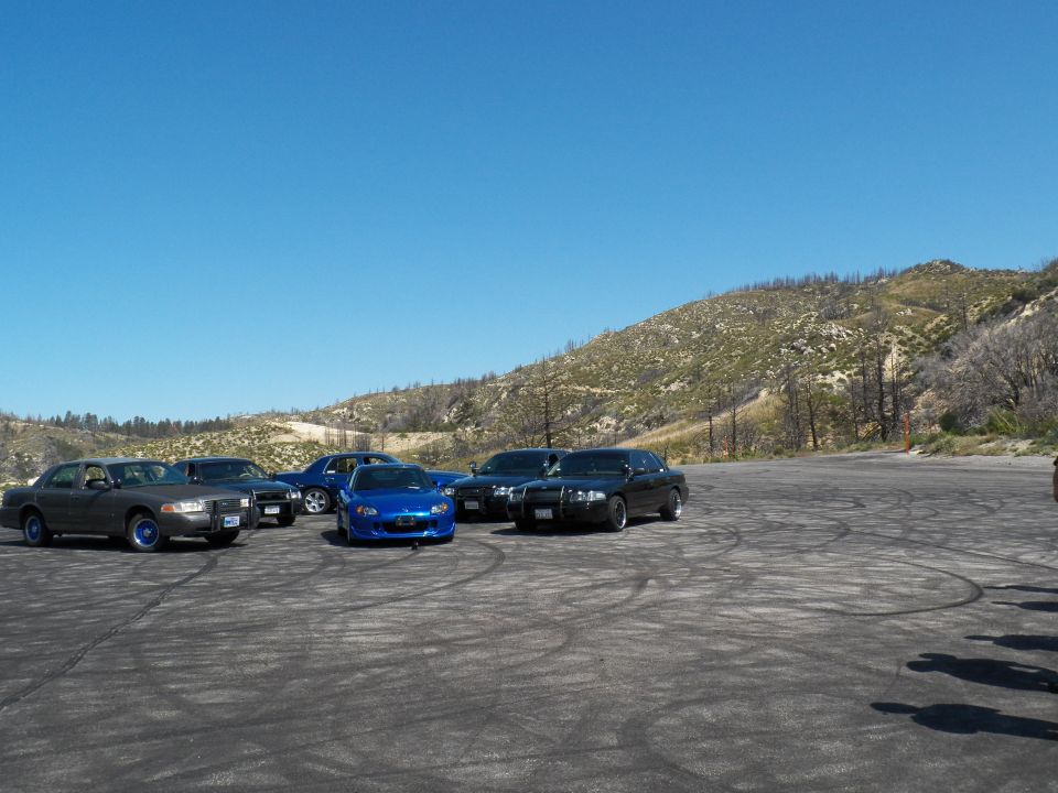 Blue Honda roadster and dark sedans lined along the edge of a wide gravel lot