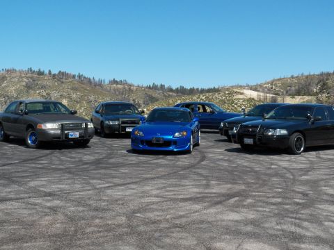 2003 Ford Crown Victoria - Group of cars parked on a dirt mountain pullout, blue roadster center with black sedans on each side