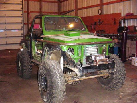 1992 Ford Bronco - A heavily modified green off-road vehicle sits in a garage, appearing to be undergoing construction or repair.