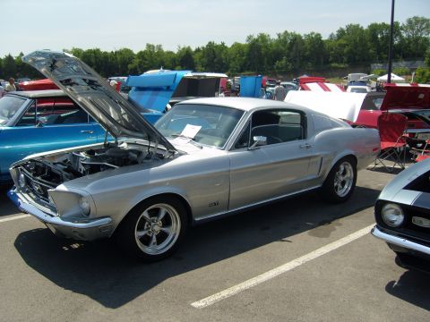 2007 Ford Mustang - Silver 1967-1968 Ford Mustang fastback at a car show, hood up, with other vehicles around.
