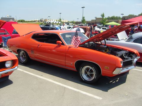 2007 Ford Mustang - Orange 1970 Ford Torino GT at a car show, hood and trunk open, with an American flag on the fender.