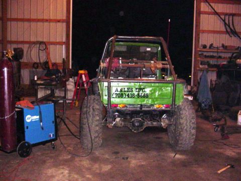1992 Ford Bronco - A custom green off-road vehicle is shown from the rear in a workshop setting, a roll cage and large tires.