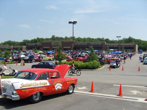 2007 Ford Mustang - A vintage custom sedan with racing-themed decals is displayed at a car show alongside numerous other vehicles.