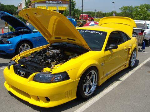 2007 Ford Mustang - A yellow Ford Mustang is parked with its hood and trunk open, revealing its engine and a supercharger.