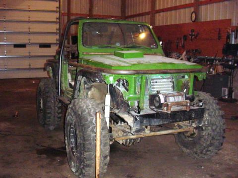 1992 Ford Bronco - A heavily modified green off-road vehicle sits in a garage with its front end partially dismantled.