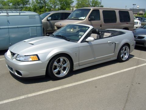 2007 Ford Mustang - A silver convertible is parked in a lot next to other vehicles, including a van and a blue camper.