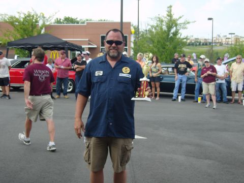 2007 Ford Mustang - A man holds a trophy at a car show event, with several vehicles and spectators visible in the background.