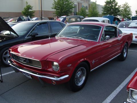 2007 Ford Mustang - A classic red Ford Mustang is displayed at an outdoor car show, with other vehicles around it.
