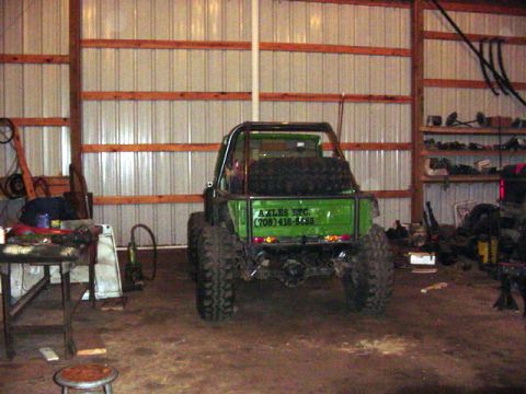 1992 Ford Bronco - A modified green off-road vehicle is parked inside a barn, showing its rear end and spare tire.