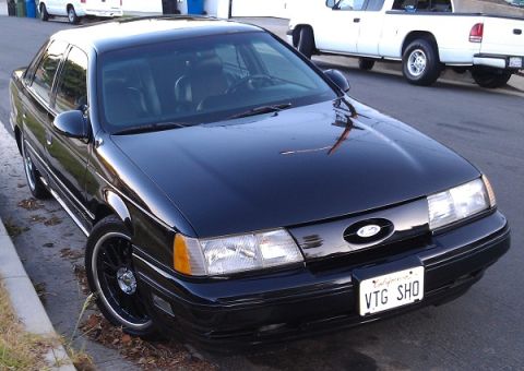 1991 Ford Taurus - A black 1991 Ford Taurus SHO is parked curbside, custom wheels and a personalized license plate.