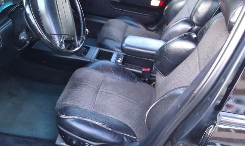 1991 Ford Taurus - The interior of a car features worn fabric and leather seats, a steering wheel, and a center console with an armrest.